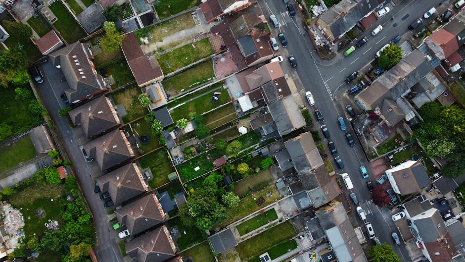 An aerial view of a residential area showing rows of terraced houses with pitched tiled roofs in varying shades of brown and gray. The houses are closely packed, separated by narrow backyards and gard